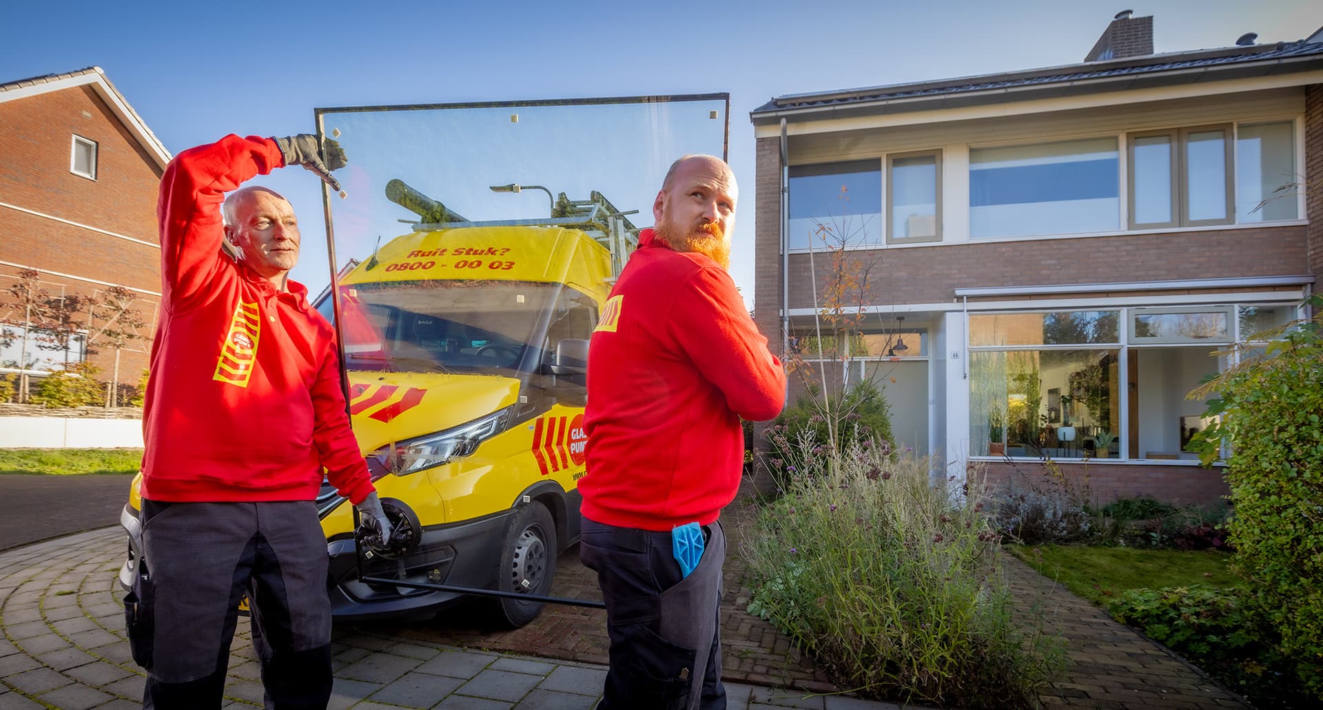 Twee glaszetters dragen een glasplaat richting een woning.