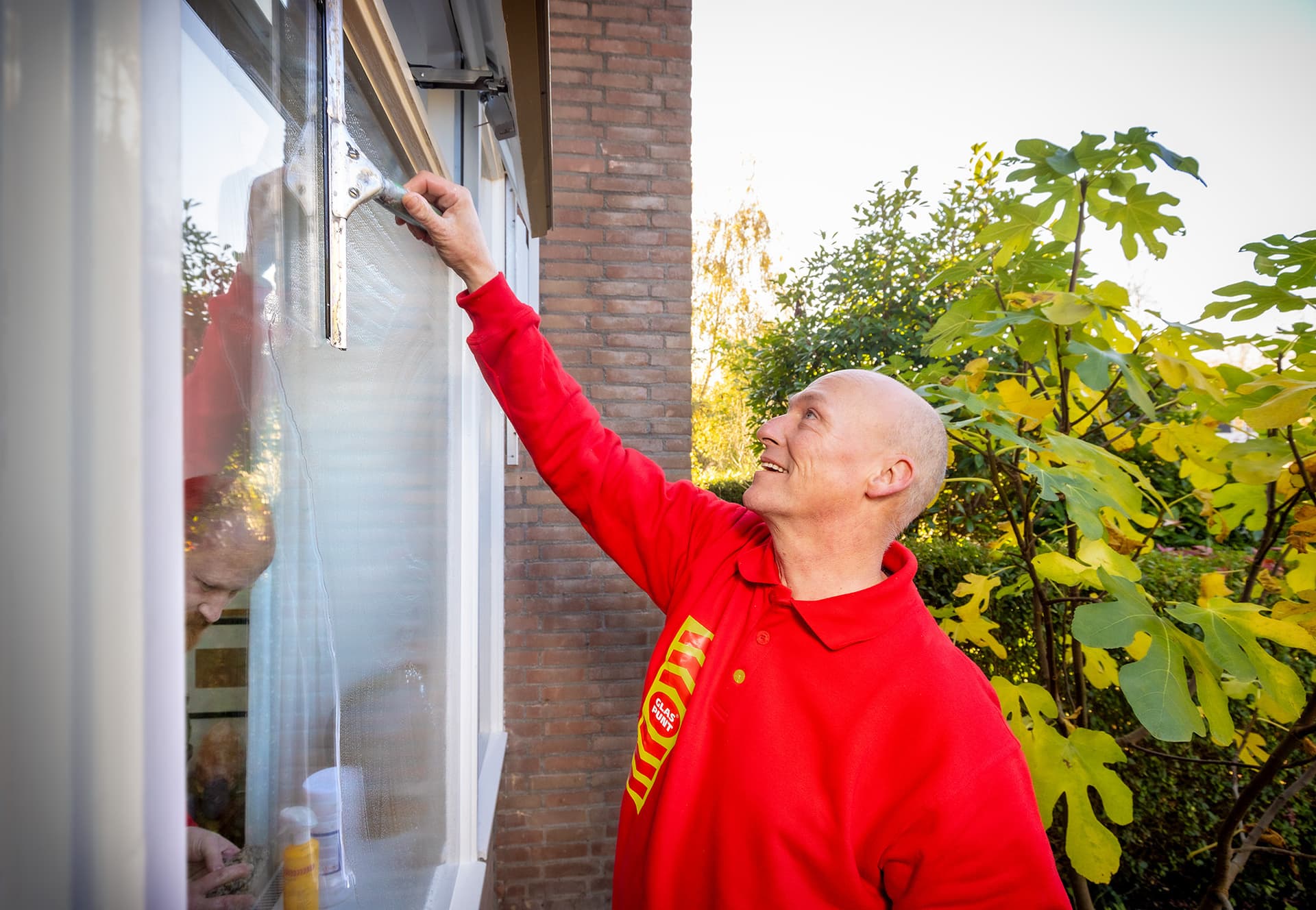 Glaszetter maakt een raam schoon met een raamtrekker.